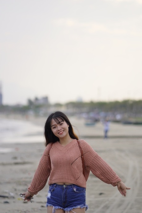 Una splendida ragazza asiatica posa in pantaloncini di jeans e maglione in pubblico