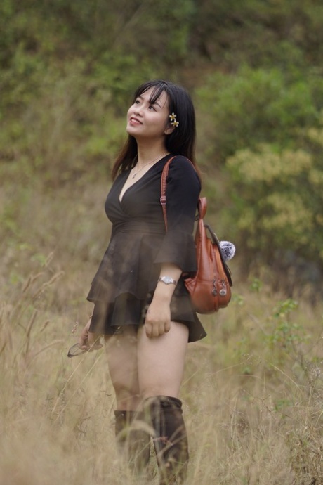 Великолепная азиатская малышка позирует в черном платье и сапогах на природе
