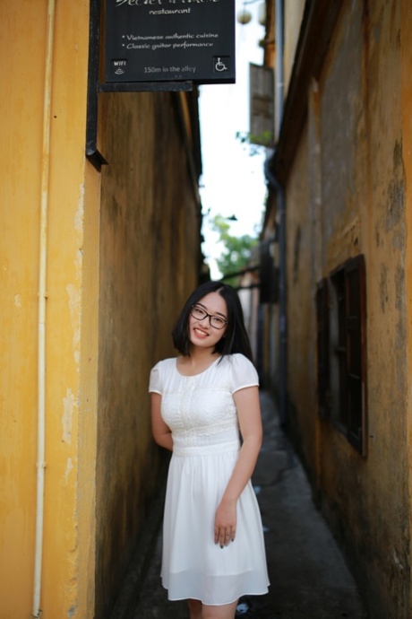 Linda chica asiática con gafas posando en su precioso vestido blanco en público