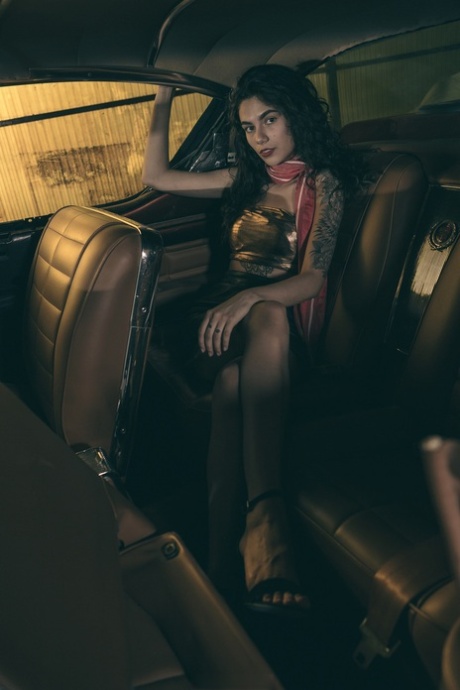 Une brune sexy pose dans sa robe et ses talons dans la voiture.