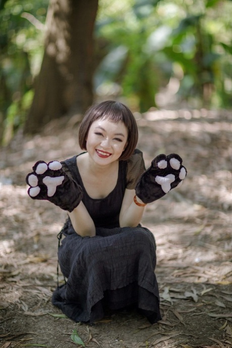 Bonita modelo asiática posando con su elegante vestido negro en el bosque