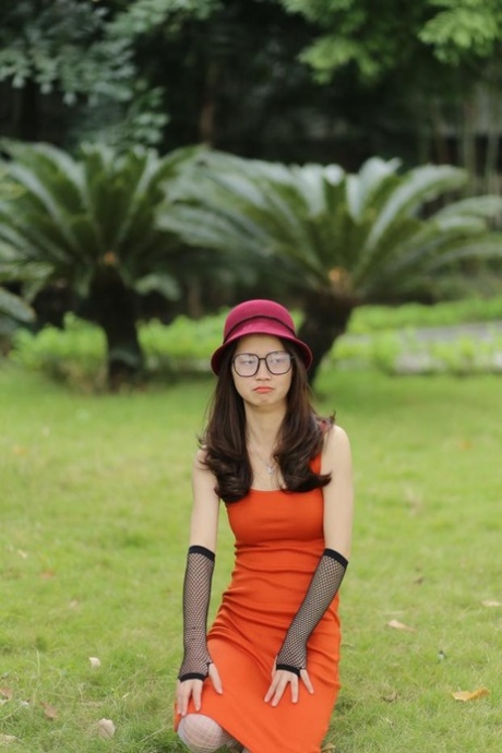 Glamorous Asian girl with a hat & glasses Maya poses in her orange dress