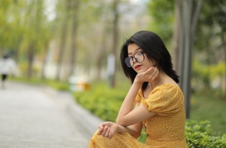 Short Asian girl with glasses Irena poses in her yellow summer dress in public