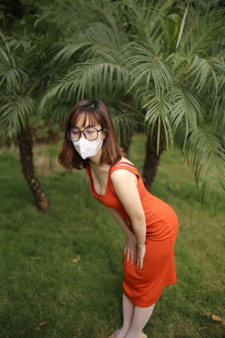 Masked Asian model with glasses posing in her tight orange dress