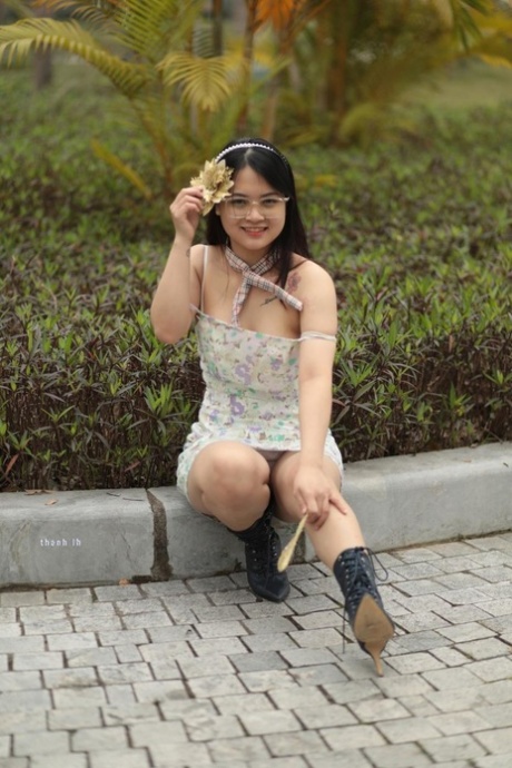 Sexy Asian girl plays with a flower while wearing a short dress and glasses
