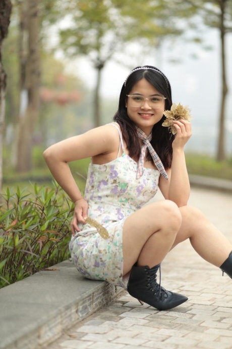 Sexy Asian girl plays with a flower while wearing a short dress and glasses