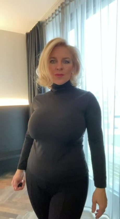 Blåögd mogen blondin visar upp sin sexiga kurviga kropp när hon poserar i fönstret