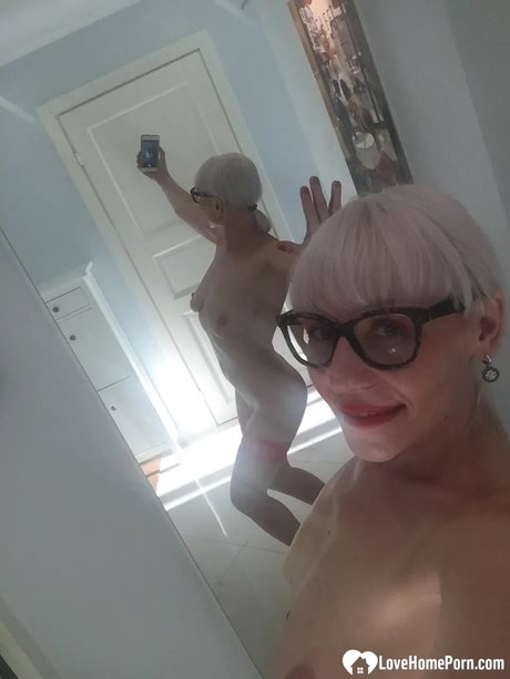 Reife Blondine zieht sich nackt aus und zeigt ihre großen Titten, während sie Aktfotos macht