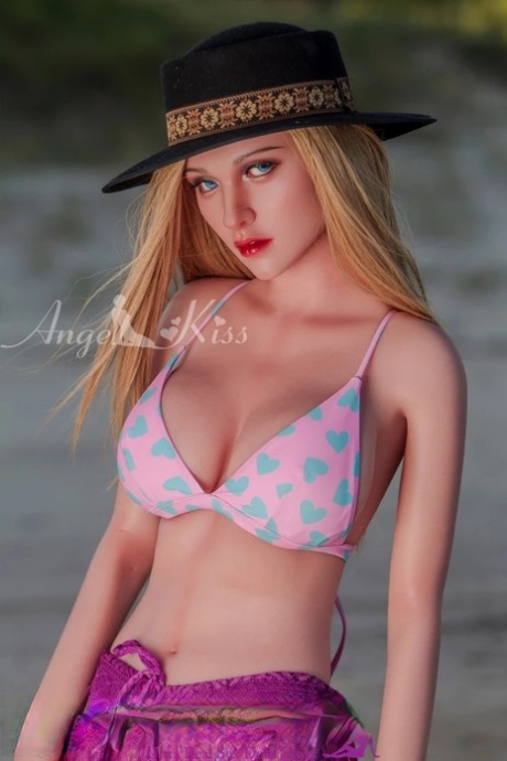 Slim silicone sex doll with a hat shows off her lovely big juggs on the beach